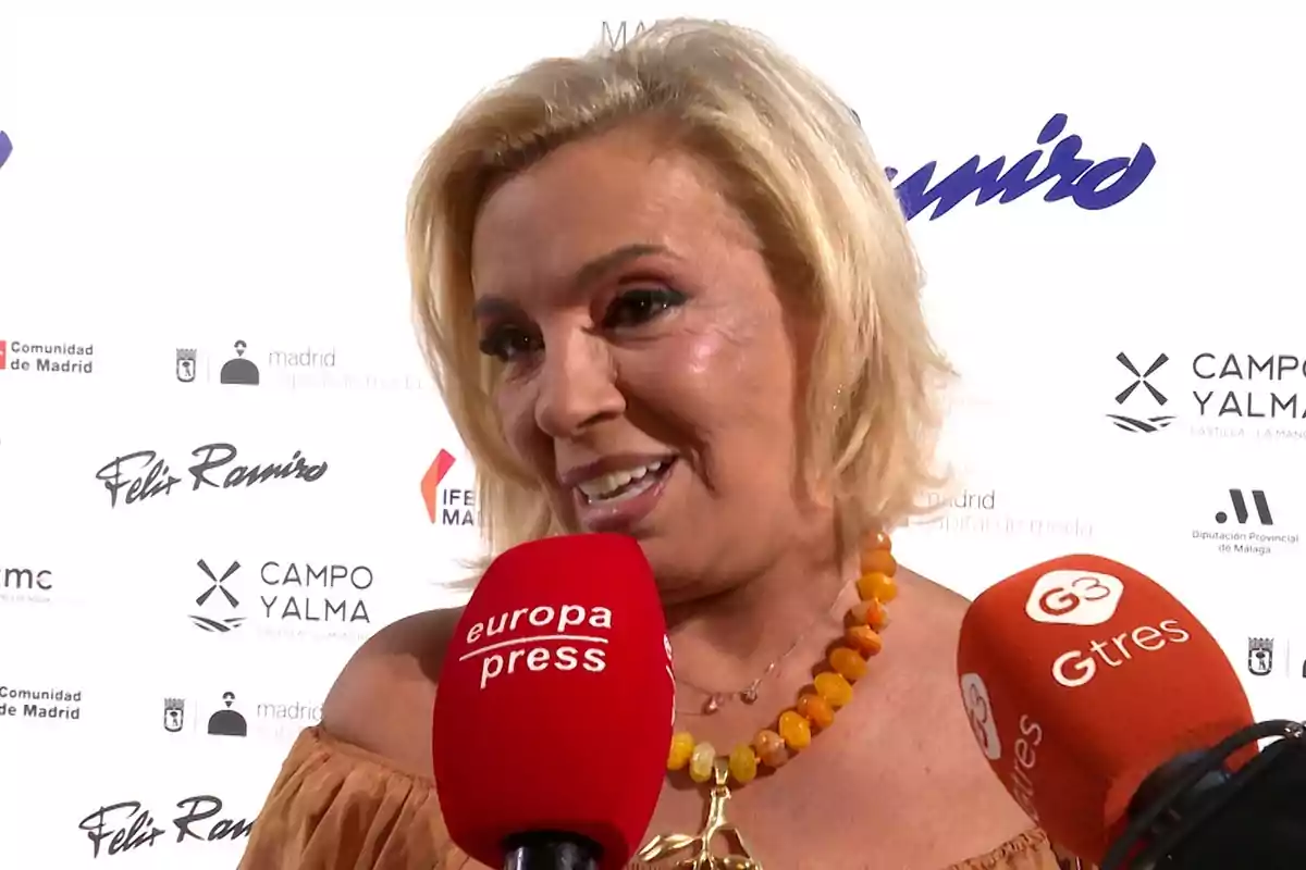 Carmen Borrego somrient donant una entrevista davant de diversos micròfons en un esdeveniment amb un fons de logotips. Carmen Borrego somrient donant una entrevista davant de diversos micròfons en un esdeveniment amb un fons de logotips.