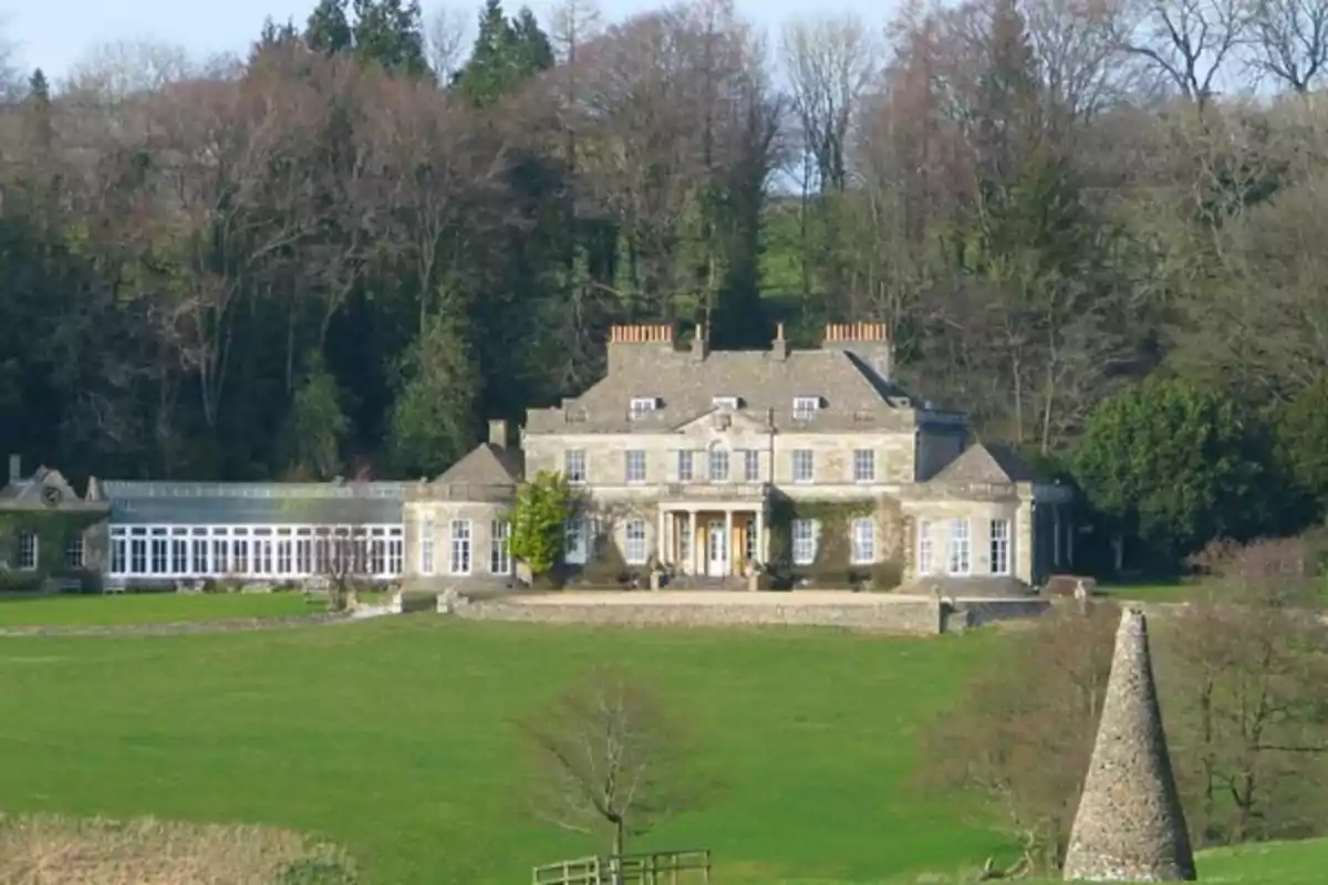 Mansión Gatcombe Park de piedra rodeada de césped verde y árboles al fondo Mansión Gatcombe Park de piedra rodeada de césped verde y árboles al fondo