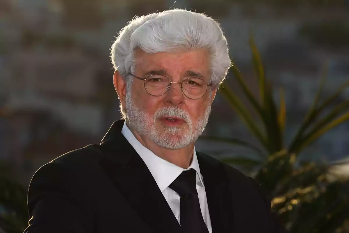 George Lucas de cabell i barba blanca amb ulleres i vestit fosc posant a l’aire lliure amb plantes i fons desenfocat George Lucas de cabell i barba blanca amb ulleres i vestit fosc posant a l’aire lliure amb plantes i fons desenfocat