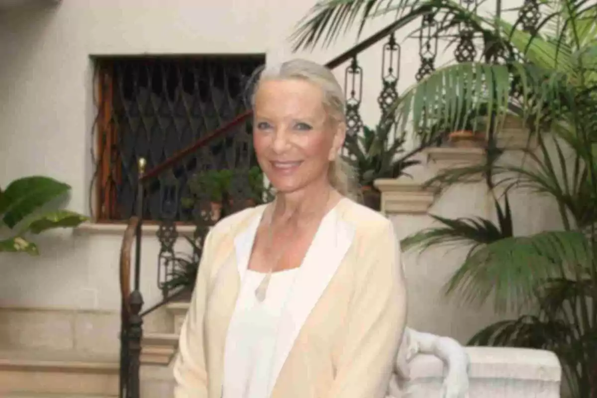 La duquesa de Kent somrient, vestida amb roba clara, posant en un ambient interior amb plantes i una escala al fons