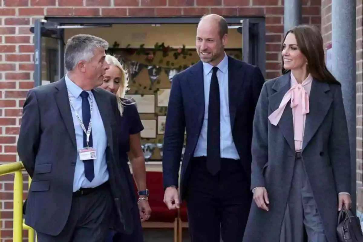 Kate Middleton i el príncep Guillem elegantment vestits caminen i conversen somrients davant d’un edifici de maó vermell.