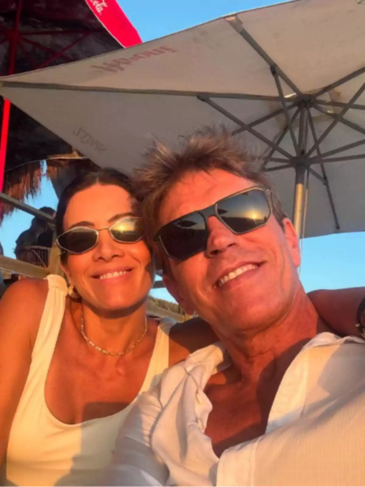 Manuel Díaz 'El Cordobés' y Virginia Troconis sonriendo usando gafas de sol disfrutando de un día soleado al aire libre bajo una sombrilla