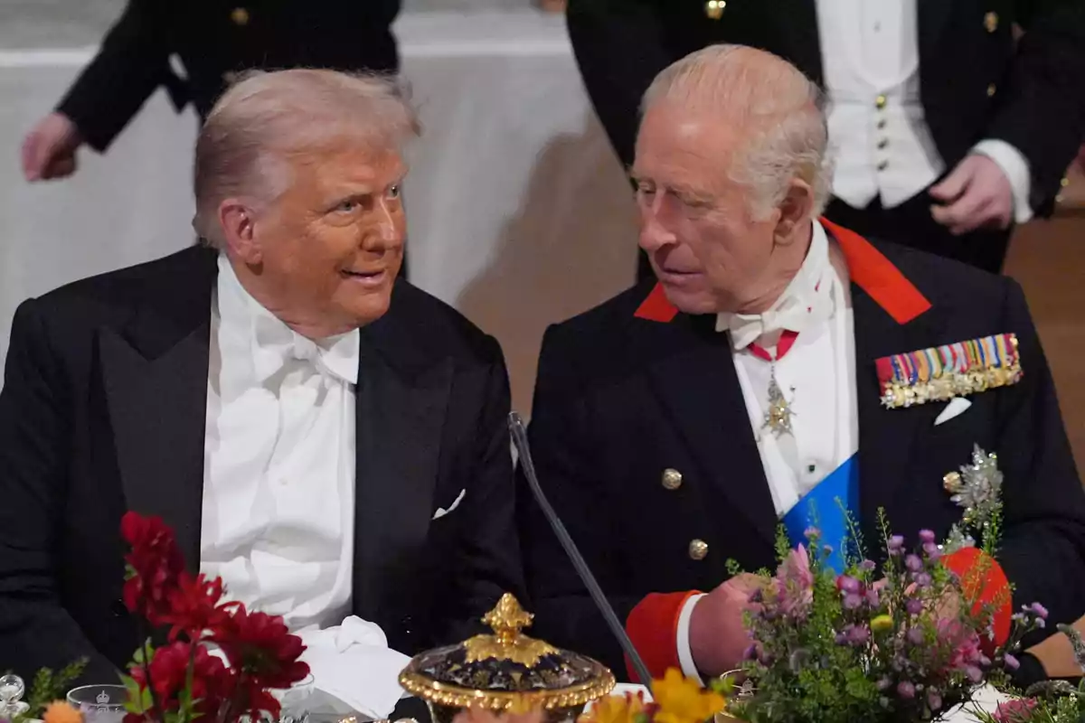 Donald Trump i el rei Carles III conversen asseguts en una taula decorada amb flors i vaixella fina.