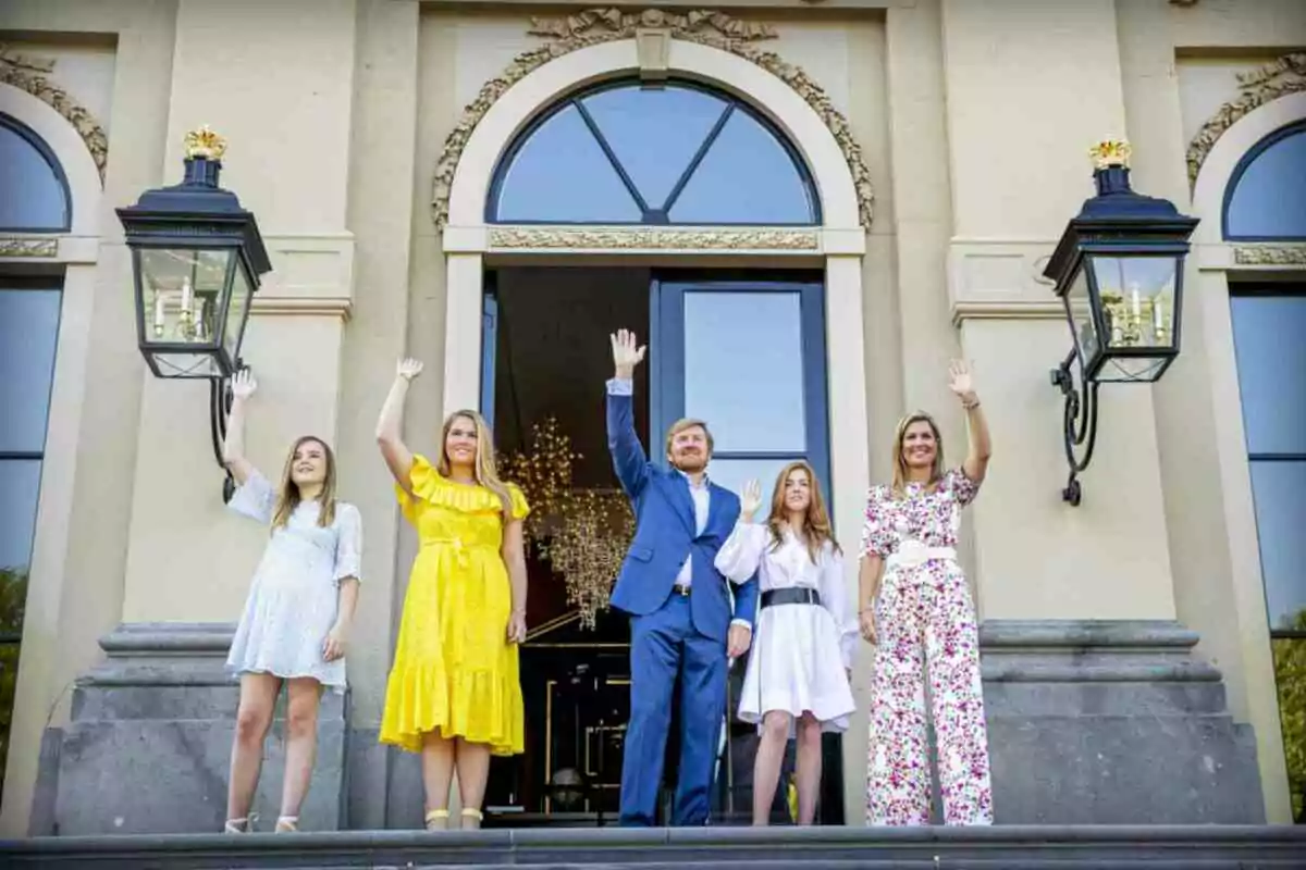 Royal Family from the Netherlands standing at the entrance of an elegant building wave by raising their hands.