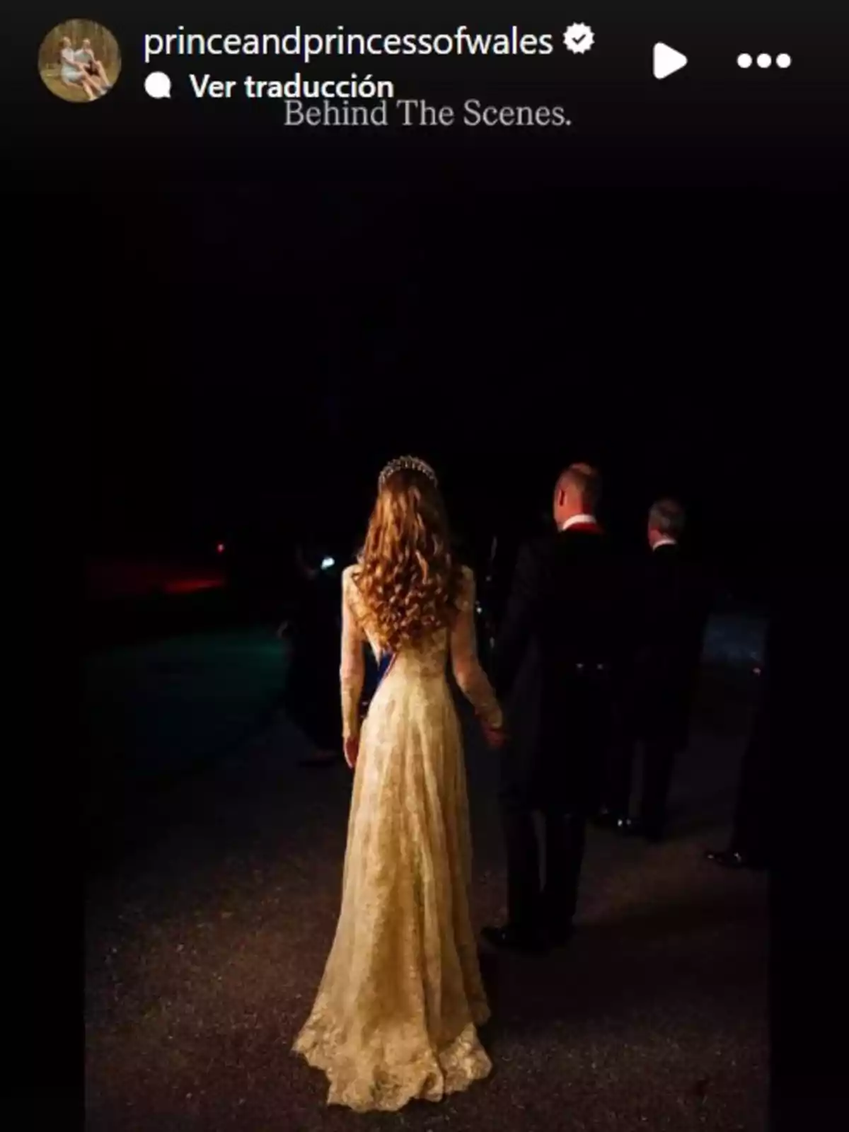 Kate Middleton amb vestit llarg i daurat d’esquena caminant al costat del príncep Guillem en un ambient fosc i elegant