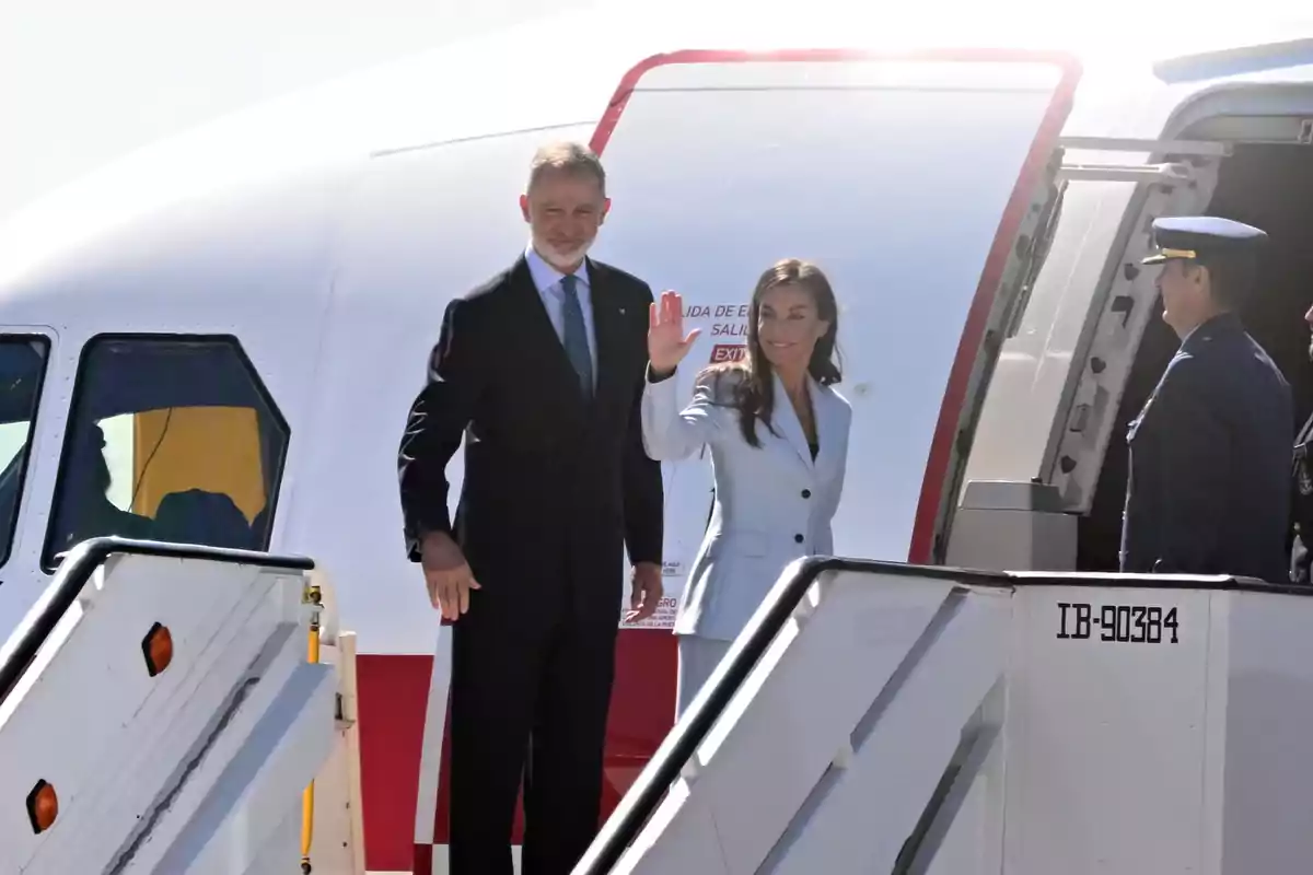 La reina Letícia saluda amb la mà mentre puja a un avió acompanyada del rei Felip i personal militar els espera al peu de l’escala.