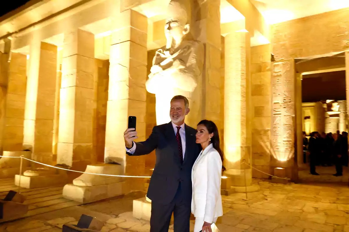 Els reis Felip i Letícia elegantment vestits es fan una selfie davant d’un temple egipci il·luminat a la nit. Els reis Felip i Letícia elegantment vestits es fan una selfie davant d’un temple egipci il·luminat a la nit.