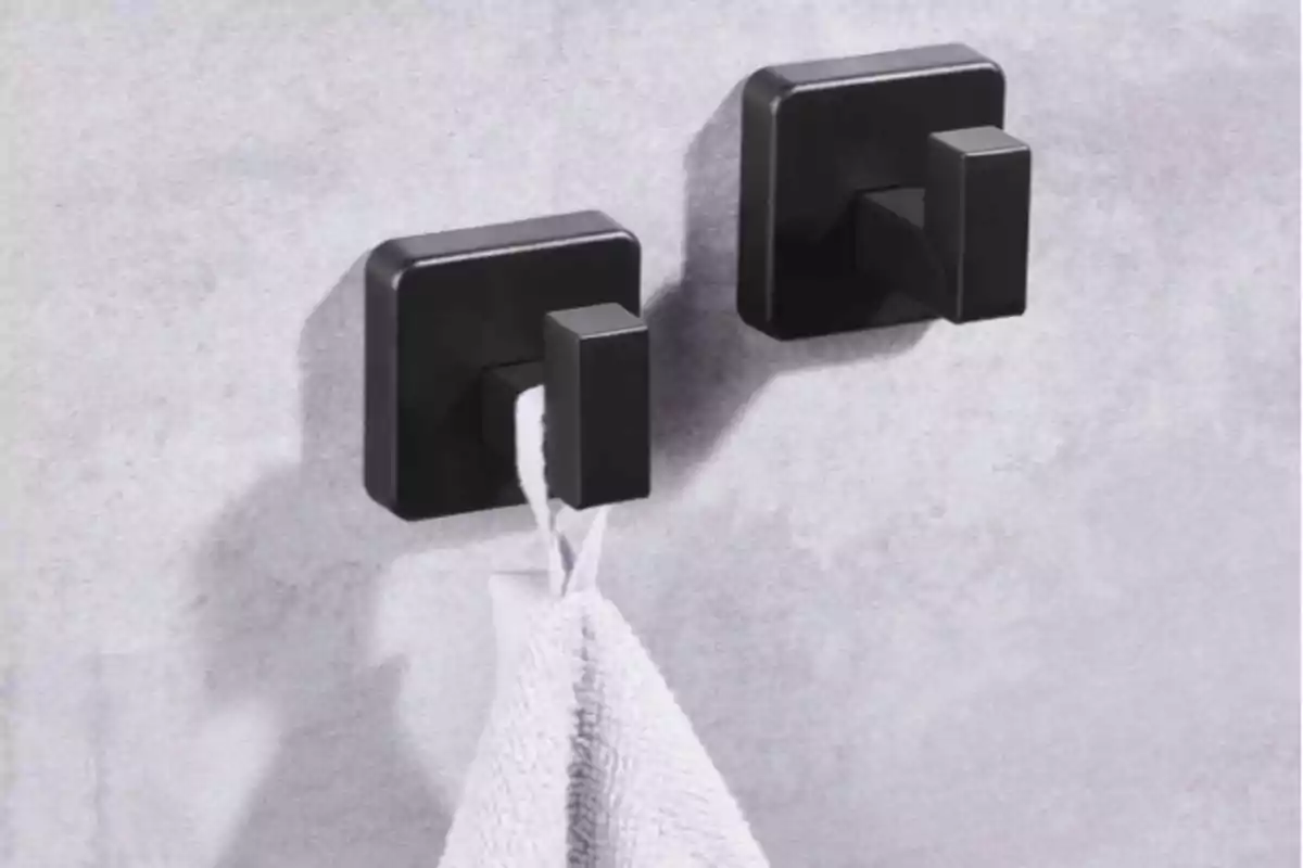 Dos ganxos quadrats negres a la paret sostenint una tovallola blanca