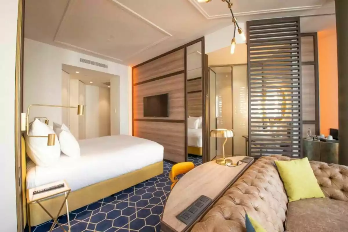 Habitació d’hotel moderna amb llit gran, sofà entapissat, escriptori de fusta, làmpades daurades i decoració elegant Habitació d’hotel moderna amb llit gran, sofà entapissat, escriptori de fusta, làmpades daurades i decoració elegant