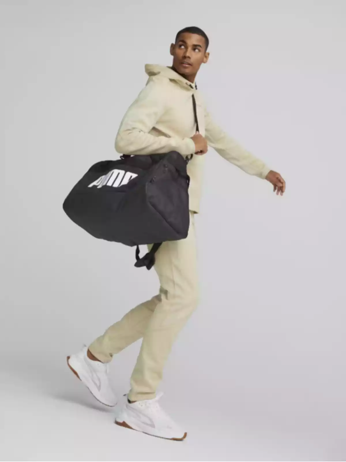 Home amb dessuadora i pantalons beix porta una bossa esportiva negra i mira cap a un costat mentre camina