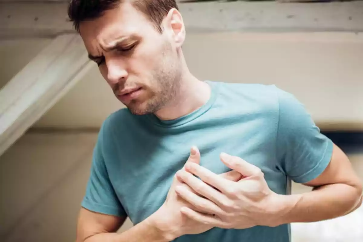 Home jove amb expressió de dolor subjectant-se el pit amb totes dues mans