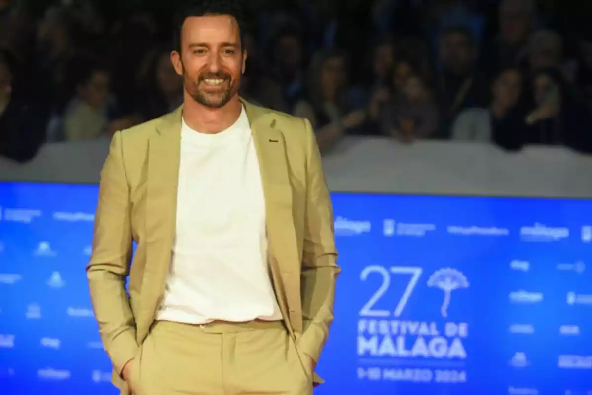 Pablo Puyol with a beard and short hair, dressed in a beige suit and white t-jersey, smiling in front of a blue background at the Málaga Festival