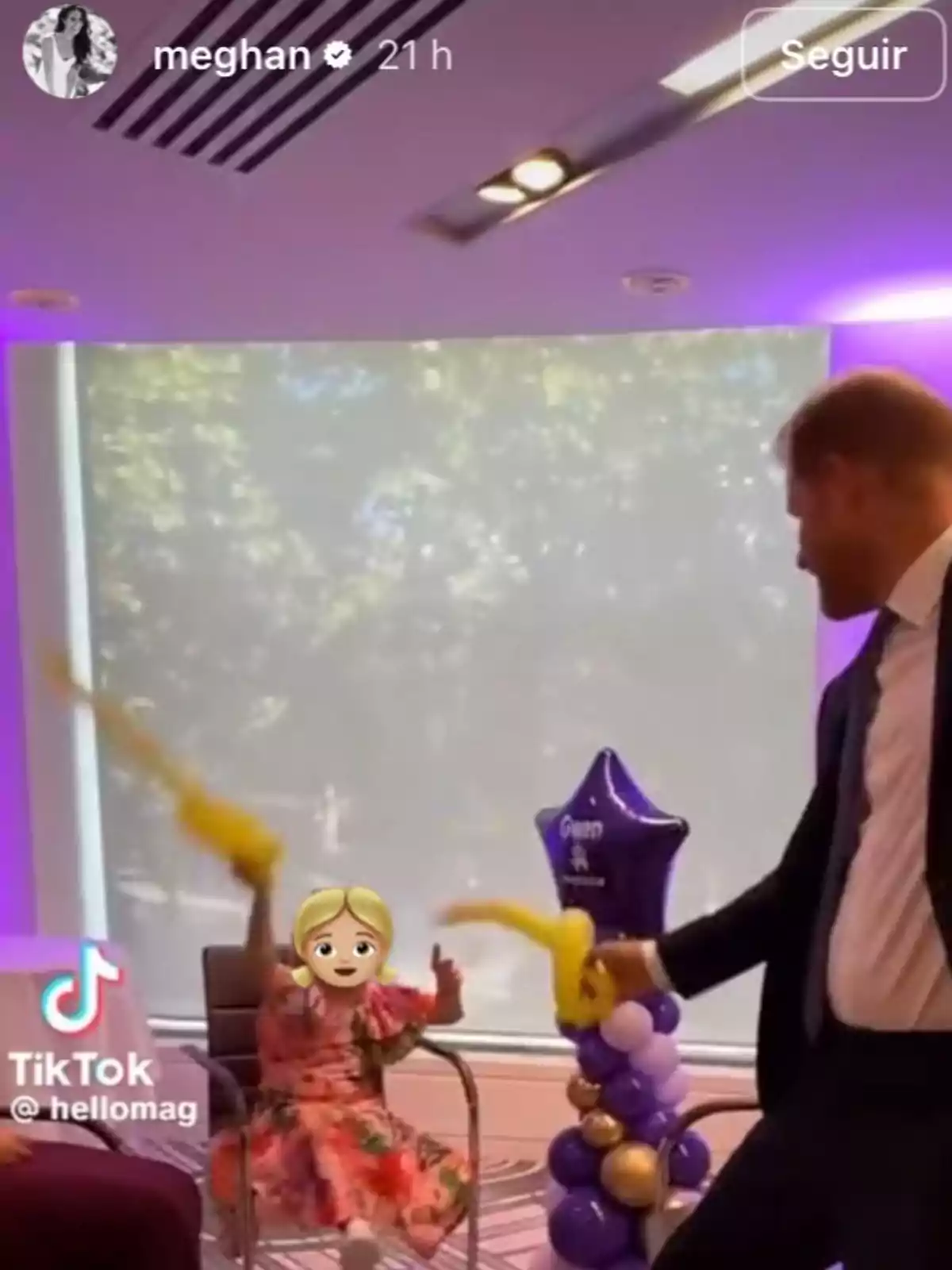 Un home amb vestit juga amb globus grocs al costat d’una nena asseguda en una cadira, el rostre de la qual està cobert amb un emoji, en una sala decorada amb globus liles i daurats. Un home amb vestit juga amb globus grocs al costat d’una nena asseguda en una cadira, el rostre de la qual està cobert amb un emoji, en una sala decorada amb globus liles i daurats.