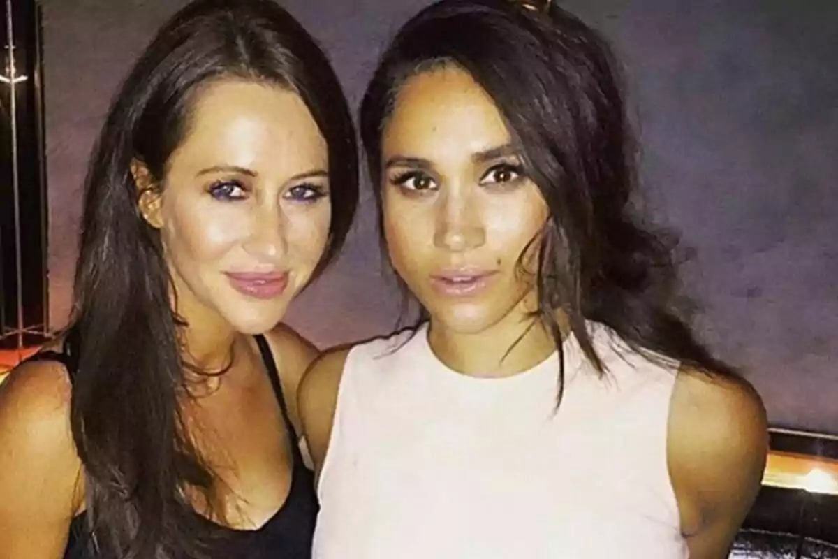 Dues dones joves posen juntes i somriuen en un ambient interior amb llum tènue.