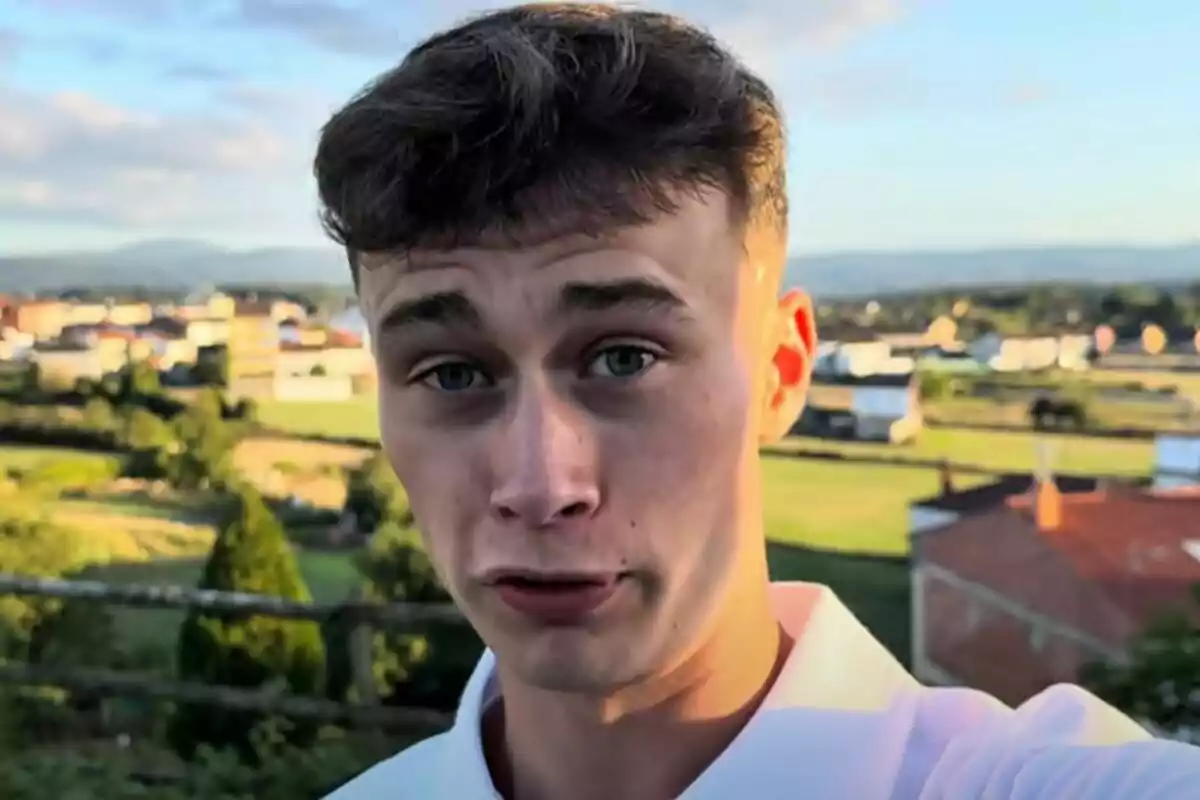 Plano corto de Jorge Rey con camisa blanca posando al aire libre con un paisaje de casas y campo al fondo. Plano corto de Jorge Rey con camisa blanca posando al aire libre con un paisaje de casas y campo al fondo.