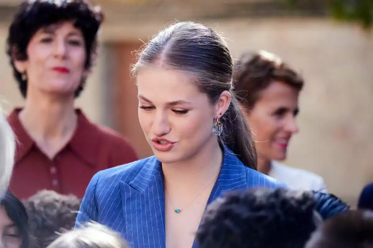 Jove amb jaqueta blava i cabell recollit interactuant amb un grup de persones en un ambient a l’aire lliure