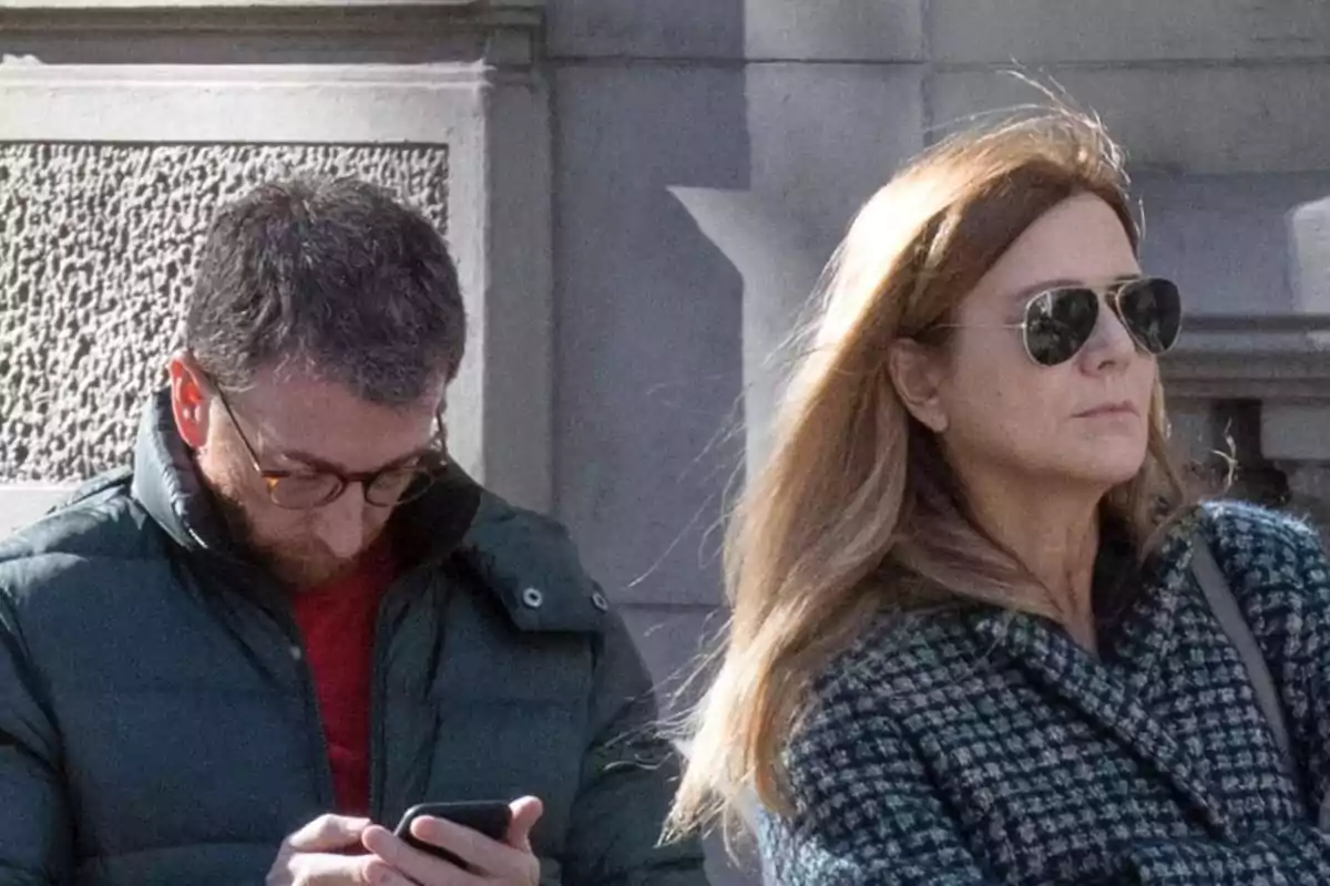Pablo Motos con gafas mira su teléfono mientras Laura Llopis con gafas de sol camina a su lado en una calle urbana Pablo Motos con gafas mira su teléfono mientras Laura Llopis con gafas de sol camina a su lado en una calle urbana