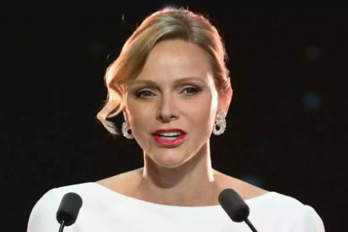 Primer pla de Charlene amb llavis vermells i vestit blanc parlant davant de dos micròfons.