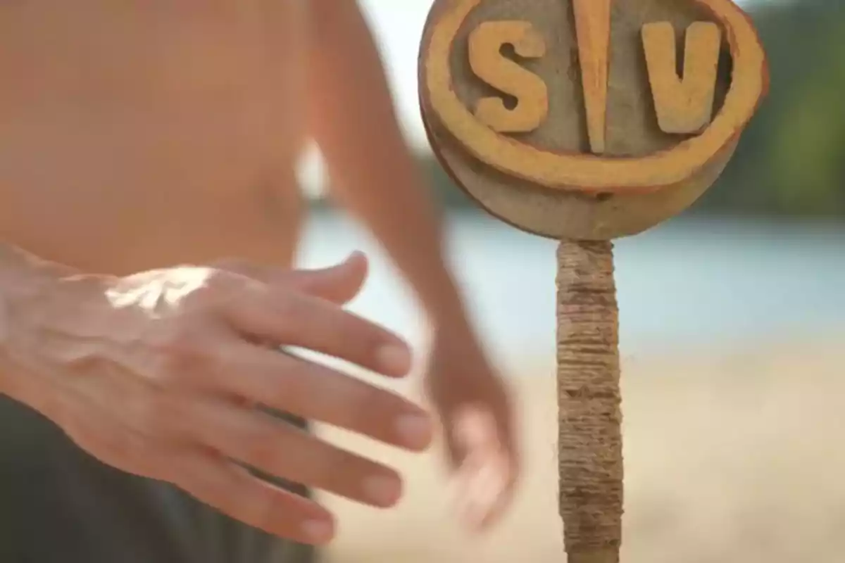 Mà estesa acostant-se a un tòtem de fusta amb les lletres SV a la platja Mà estesa acostant-se a un tòtem de fusta amb les lletres SV a la platja