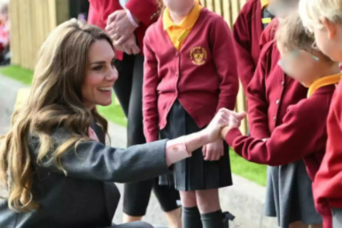 Kate Middleton somrient i saludant amb el puny a un grup de nens que porten uniforme escolar vermell.