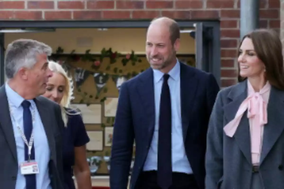 Quatre persones elegantment vestides conversen i somriuen mentre caminen davant d’un edifici de maó, dues d’elles són la Kate Middleton i el seu marit.