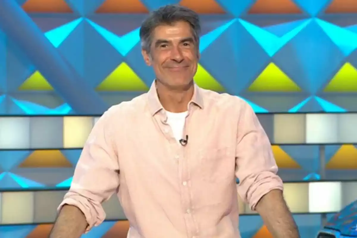 Jorge Fernández amb camisa clara somriu davant d’un fons acolorit amb figures geomètriques. Captura de ‘La Ruleta de la Suerte’.