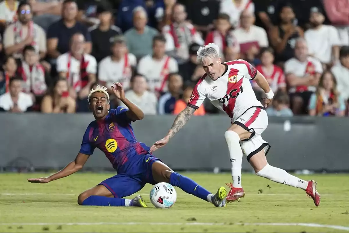 Un jugador del Barcelona cae al suelo tras una entrada de un futbolista del Rayo Vallecano durante un partido de fútbol con público en las gradas. Un jugador del Barcelona cae al suelo tras una entrada de un futbolista del Rayo Vallecano durante un partido de fútbol con público en las gradas.