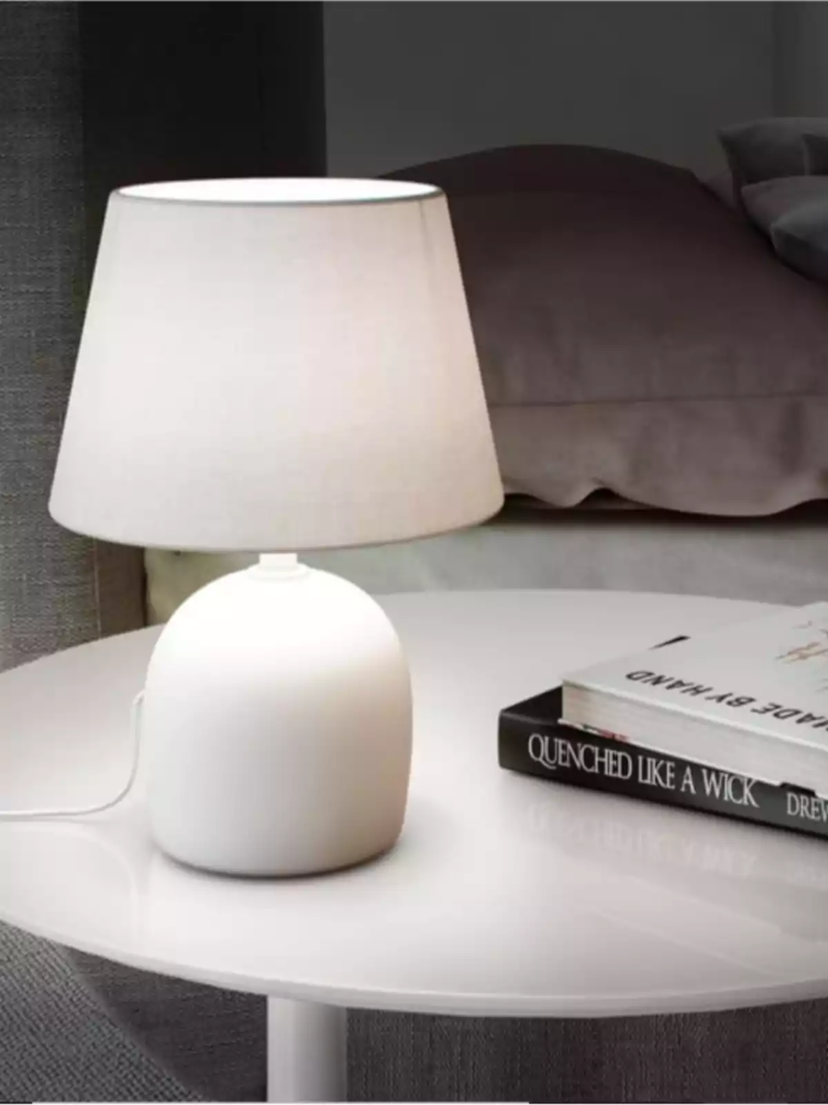 Làmpada de taula blanca encesa sobre una taula rodona al costat d’un parell de llibres en una habitació acollidora