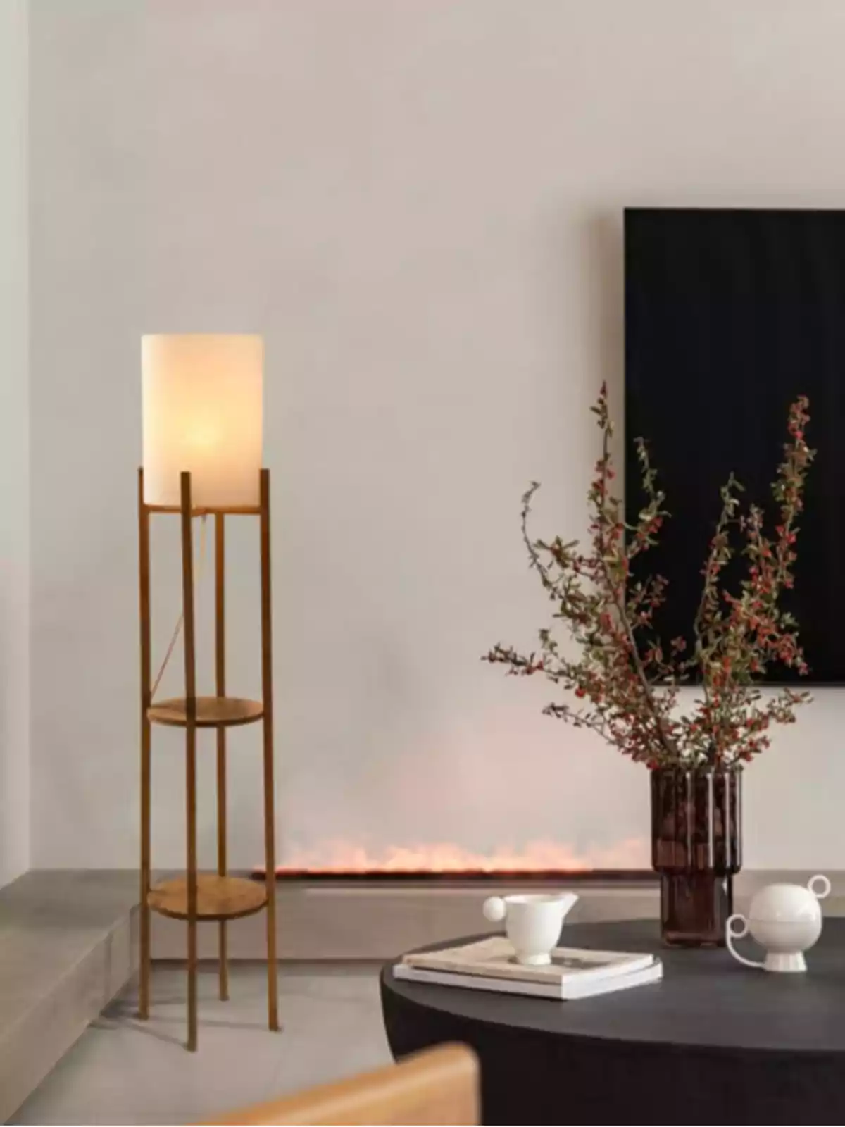 Sala moderna amb làmpada de peu encesa, taula negra amb gerro de flors i tasses blanques, fons amb llar de foc i televisor a la paret