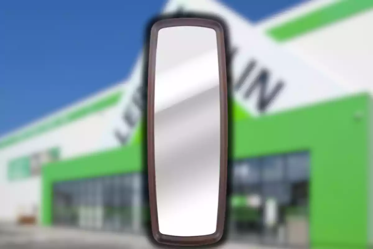 Mirall rectangular amb marc fosc davant d’un edifici amb façana verda i blanca desenfocada