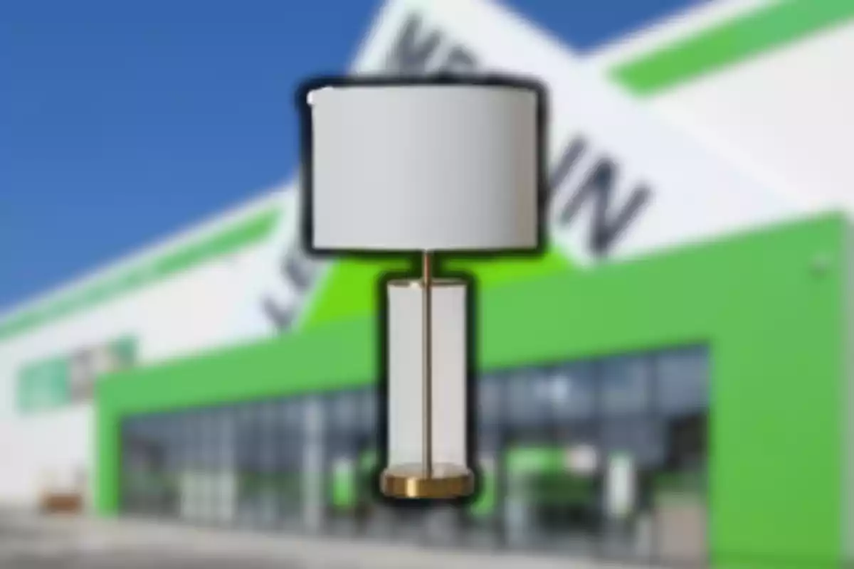 Làmpada de taula moderna amb base daurada i pantalla blanca davant d’una botiga amb façana verda i blanca desenfocada Làmpada de taula moderna amb base daurada i pantalla blanca davant d’una botiga amb façana verda i blanca desenfocada