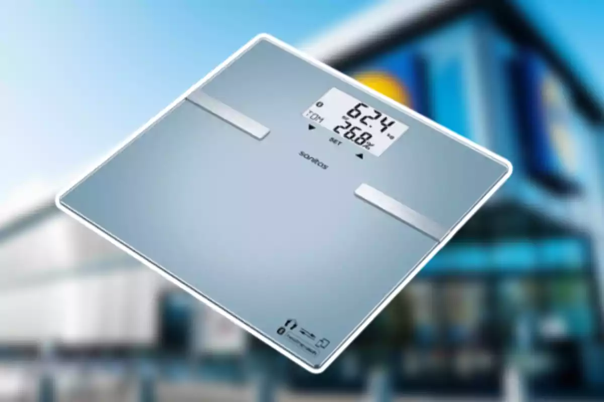 Bàscula digital de vidre amb la pantalla encesa mostrant el pes i el percentatge de greix corporal sobre un fons desenfocat d’un edifici modern Bàscula digital de vidre amb la pantalla encesa mostrant el pes i el percentatge de greix corporal sobre un fons desenfocat d’un edifici modern