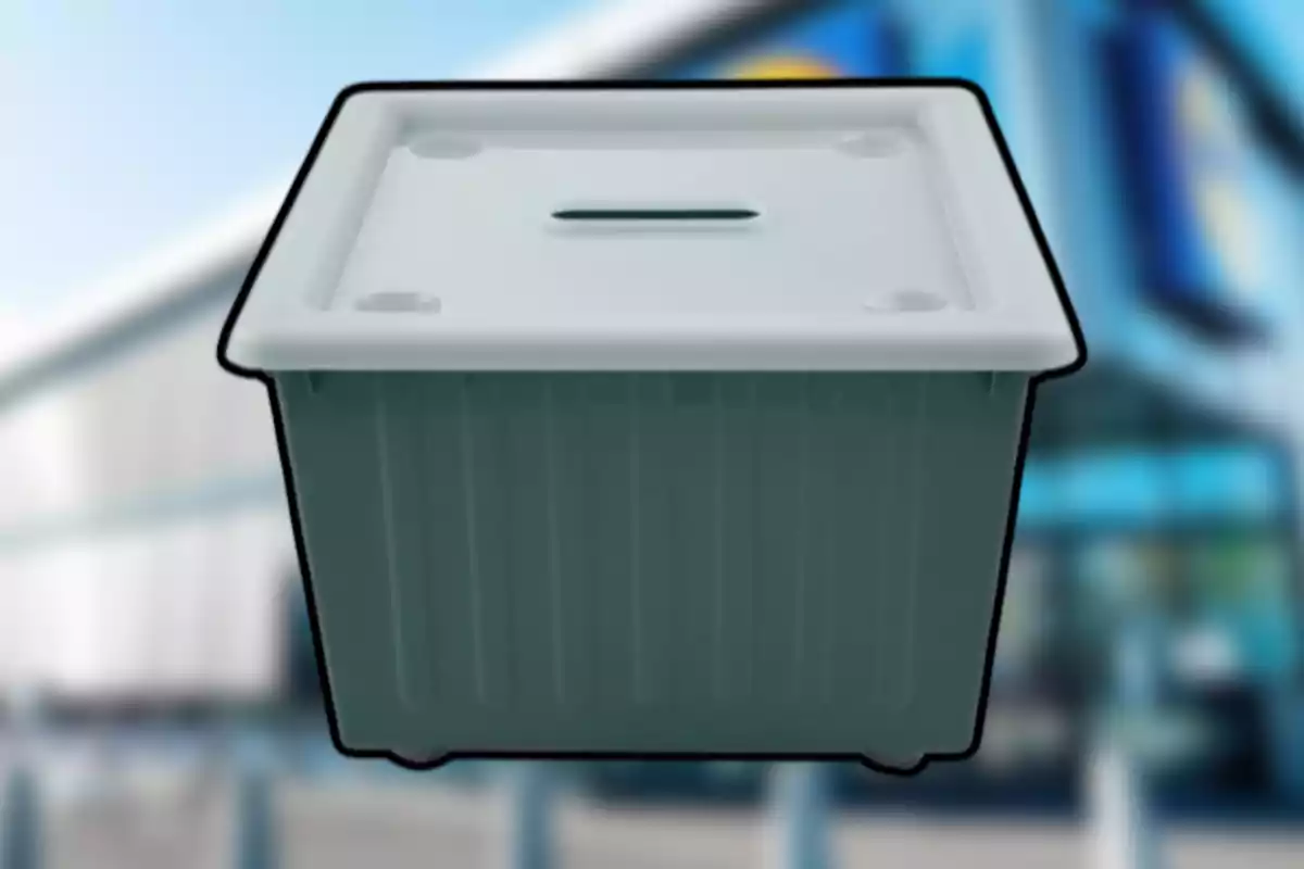 Una urna de plàstic gris amb tapa blanca i una ranura a la part superior, sobre un fons desenfocat.