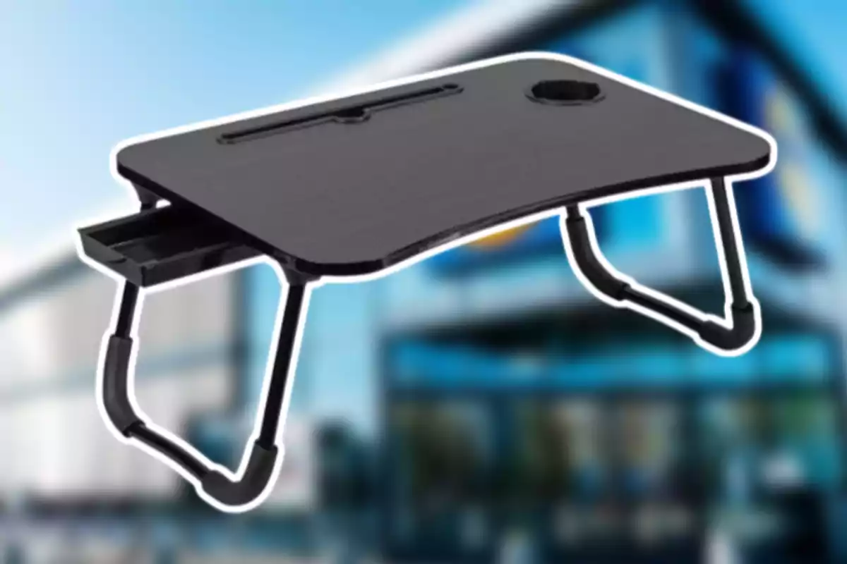 Taula portàtil negra amb potes plegables i un calaix lateral sobre un fons desenfocat d’edifici modern Taula portàtil negra amb potes plegables i un calaix lateral sobre un fons desenfocat d’edifici modern