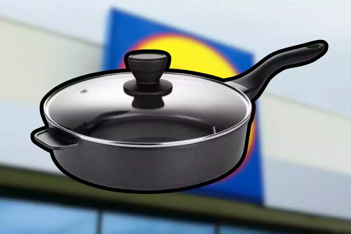 Paella negra amb tapa de vidre i mànec llarg davant d’un fons borros amb colors blau i groc