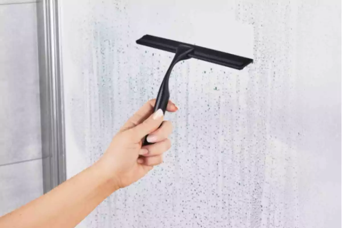 Mà utilitzant un netejavidres negre per treure l’aigua d’una superfície de vidre entelada