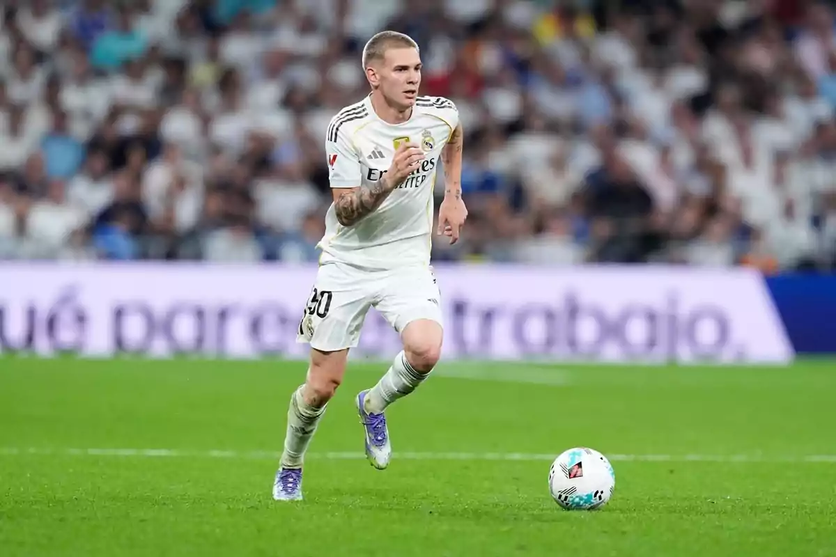 Futbolista del Reial Madrid corrent pel camp durant un partit amb la pilota a prop dels peus i el públic a les grades de fons Futbolista del Reial Madrid corrent pel camp durant un partit amb la pilota a prop dels peus i el públic a les grades de fons