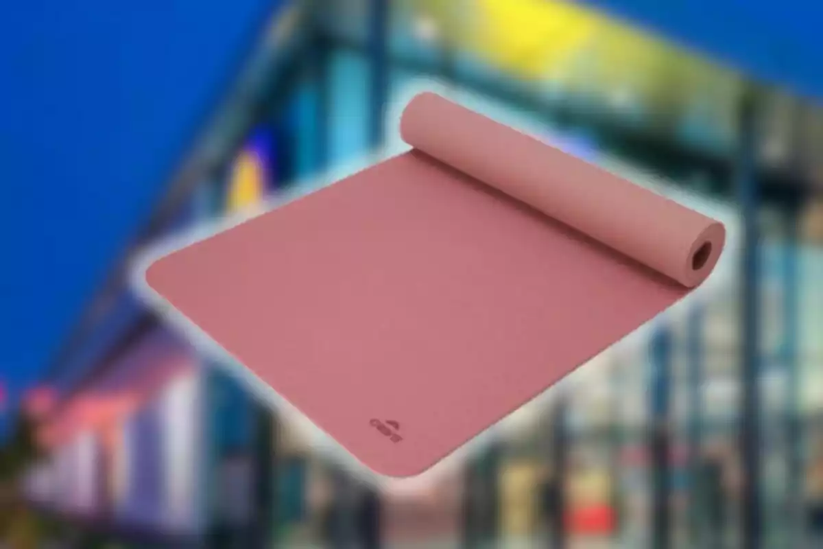 Tapete de yoga color rosa desenrollado con fondo de edificio desenfocado