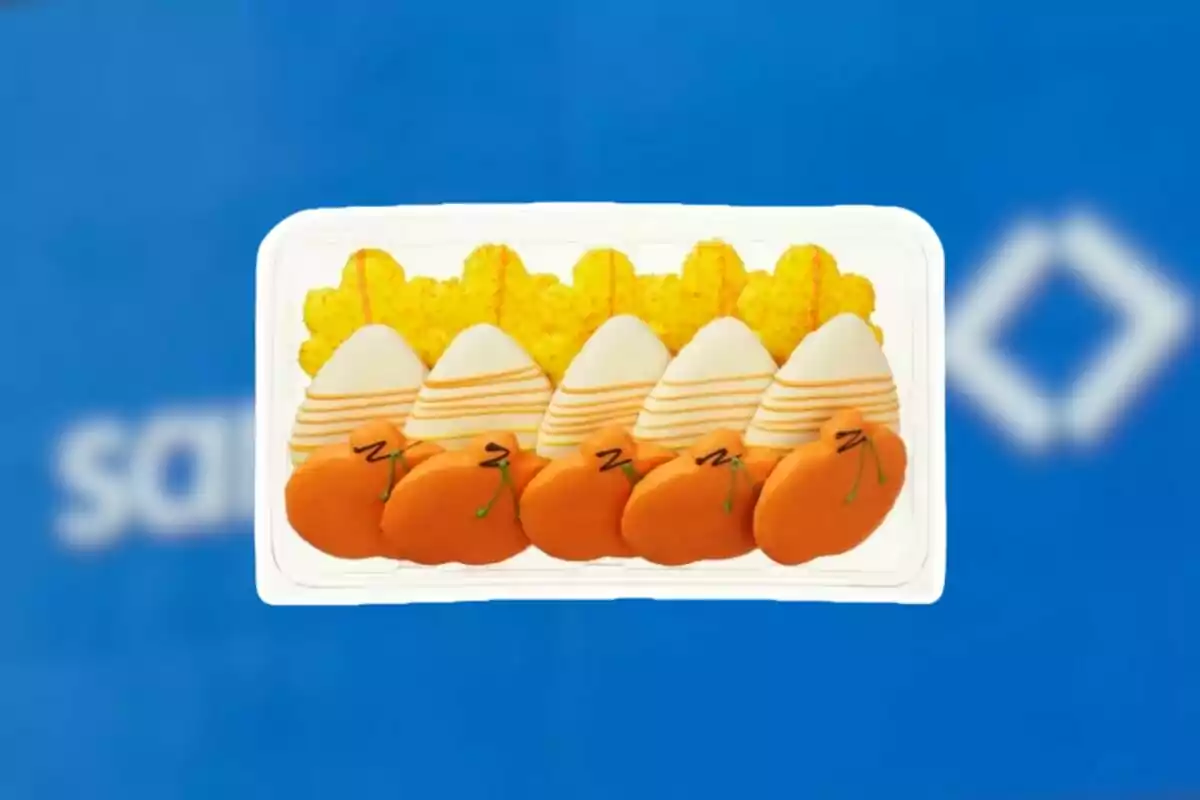 Decorated cookies shaped like carrots, eggs, and flowers on a plastic tray over a blurred blue background