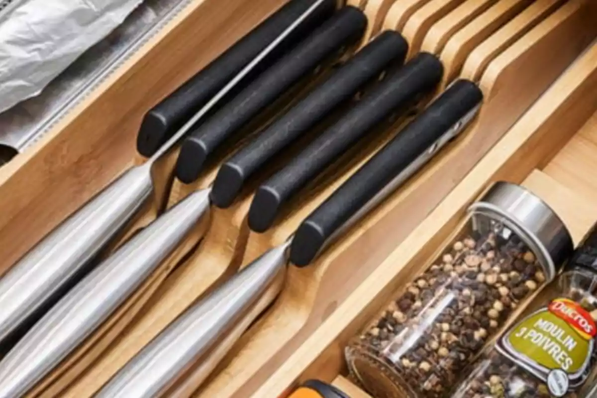 Ganivets de cuina amb mànec negre organitzats en un calaix de fusta al costat de pots d'espècies