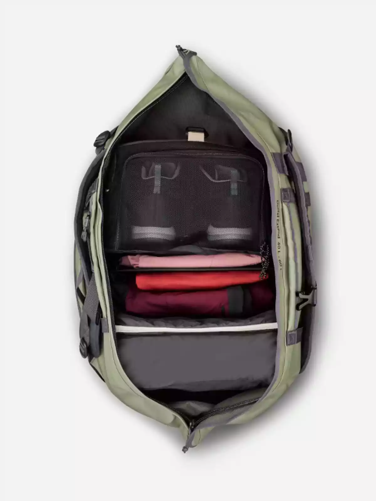 Motxilla verda oberta vista des de dalt mostrant el seu interior organitzat amb roba plegada i compartiments de xarxa negra Motxilla verda oberta vista des de dalt mostrant el seu interior organitzat amb roba plegada i compartiments de xarxa negra