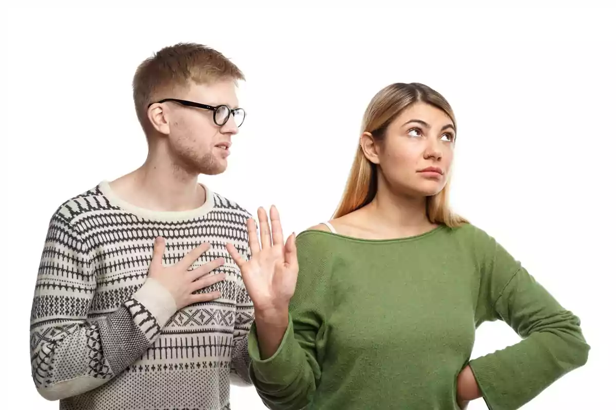 Una dona amb jersei verd sembla molesta i aixeca la mà en senyal de rebuig mentre un home amb ulleres i jersei clar intenta parlar-li.
