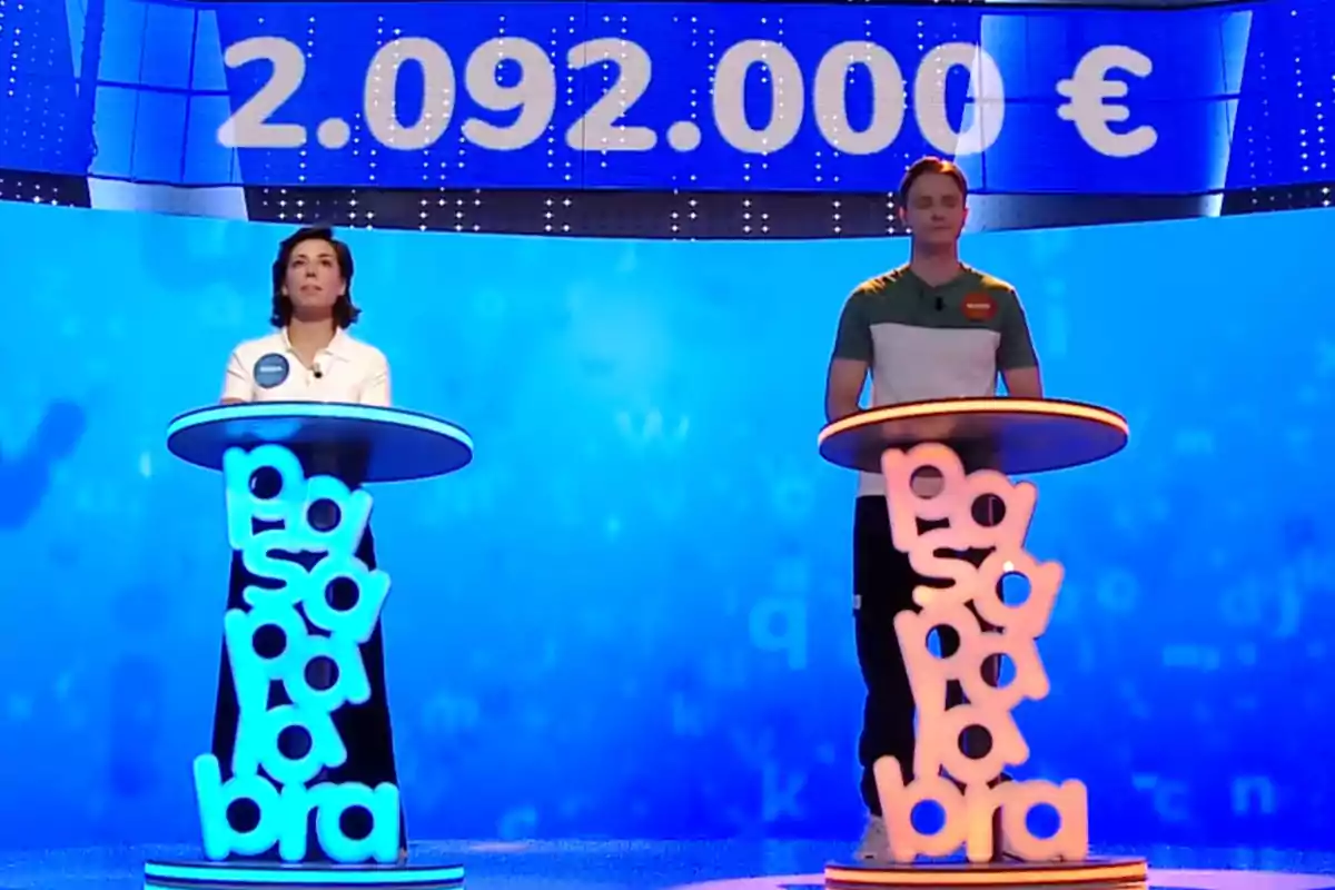 Rosa i Manu drets als seus faristols il·luminats en un plató blau d’un concurs de televisió, amb un premi de més de dos milions d’euros mostrat a la pantalla superior. Captura de ‘Pasapalabra’ Rosa i Manu drets als seus faristols il·luminats en un plató blau d’un concurs de televisió, amb un premi de més de dos milions d’euros mostrat a la pantalla superior. Captura de ‘Pasapalabra’