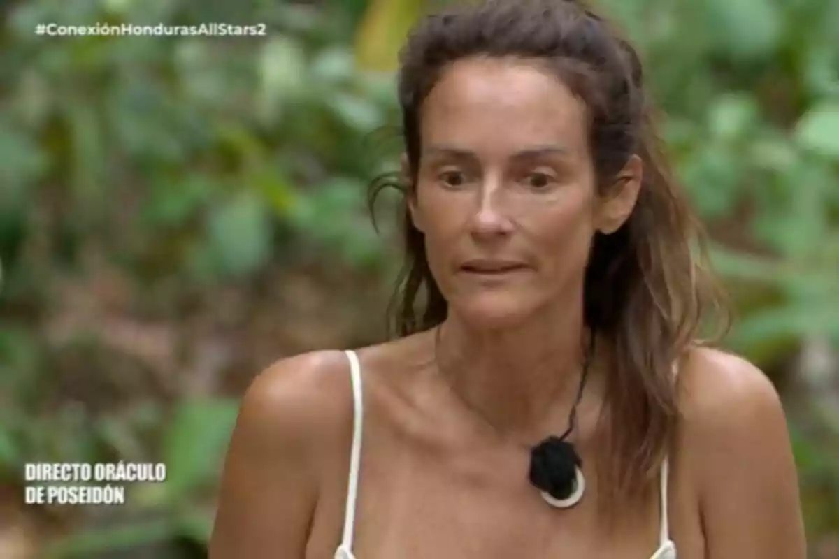 Primer pla d’Elena Rodríguez amb expressió seriosa, porta un micròfon penjat al coll i vesteix una samarreta de tirants blanca, fons de vegetació desenfocada.