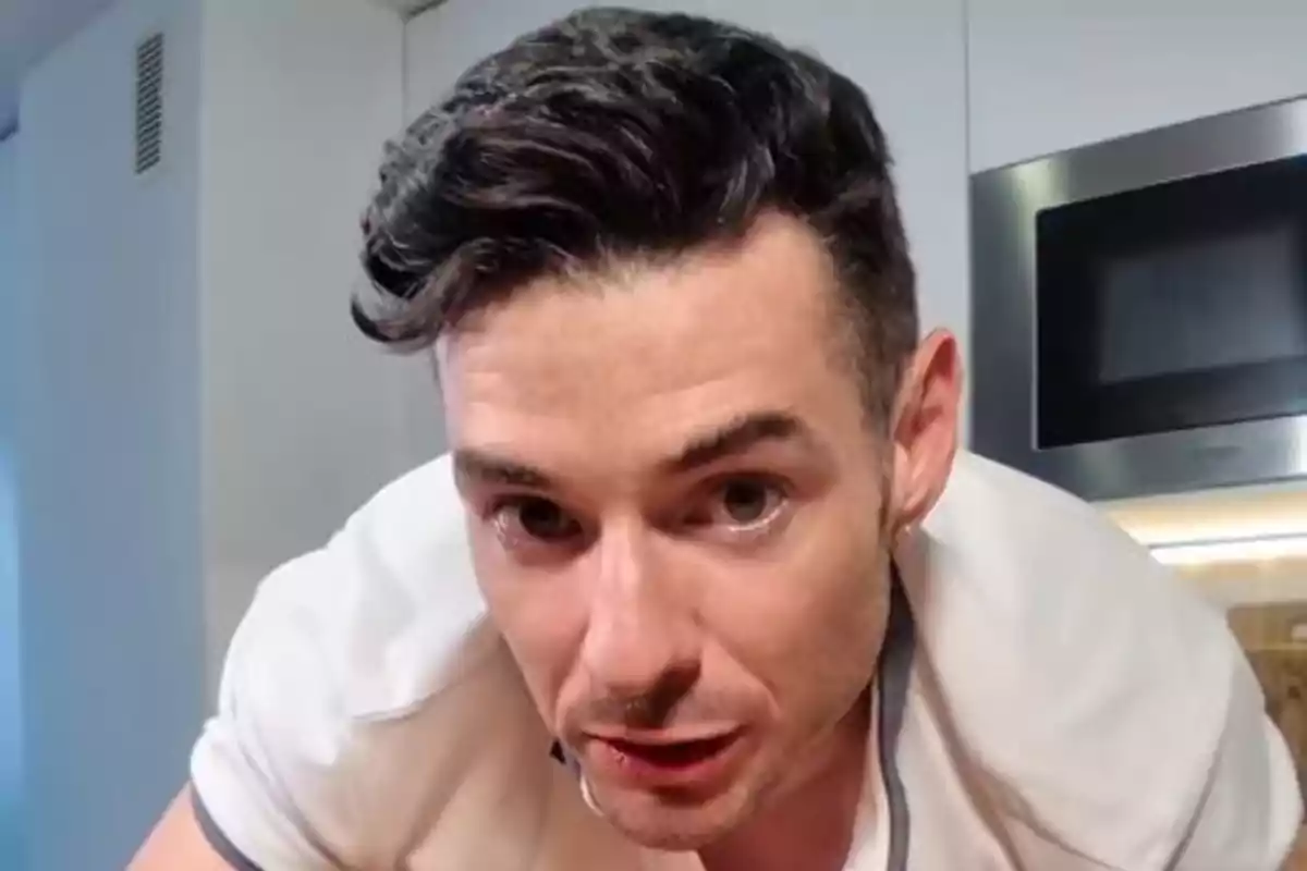 Hombre de cabello oscuro y corto inclinado hacia la cámara en una cocina moderna