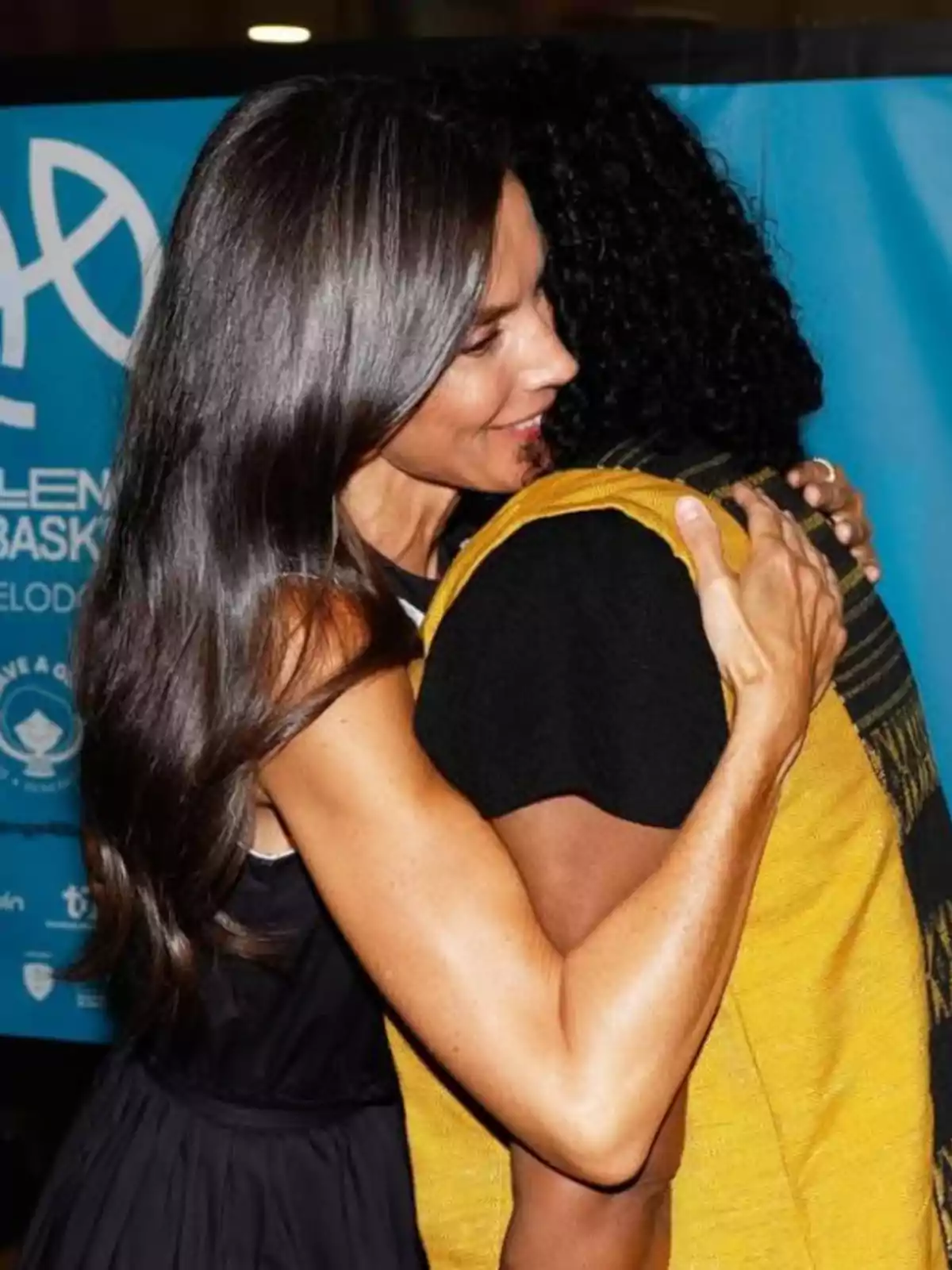 La reina Letícia i una altra dona s’abracen amb afecte davant d’un fons blau La reina Letícia i una altra dona s’abracen amb afecte davant d’un fons blau