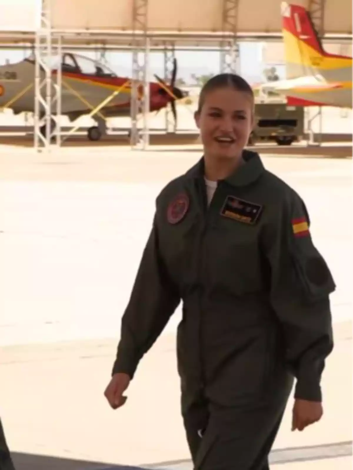 La princesa Leonor amb un vestit de vol militar verd caminant en un hangar amb avions al fons La princesa Leonor amb un vestit de vol militar verd caminant en un hangar amb avions al fons