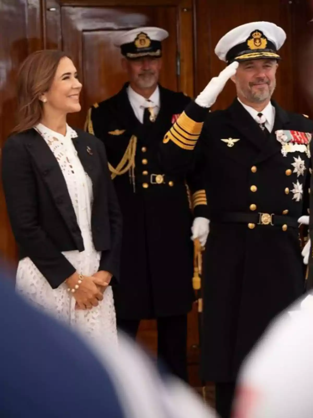 Mary de Dinamarca somrient amb vestit blanc i jaqueta fosca està dreta al costat de Frederic de Dinamarca uniformat que saluda amb la mà dreta mentre un altre home amb uniforme militar es troba al fons. Mary de Dinamarca somrient amb vestit blanc i jaqueta fosca està dreta al costat de Frederic de Dinamarca uniformat que saluda amb la mà dreta mentre un altre home amb uniforme militar es troba al fons.