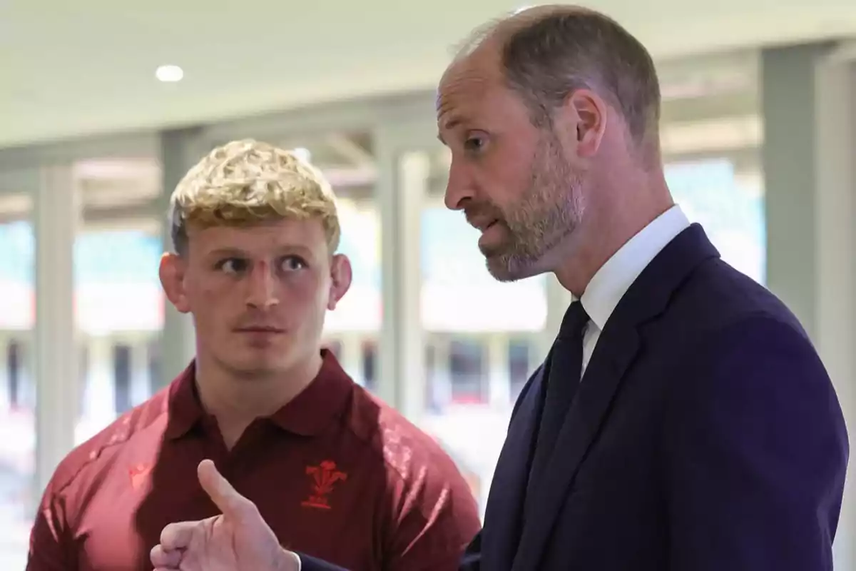 El príncep Guillem i un altre home conversen en un espai interior il·luminat, un porta un vestit fosc i l’altre porta una samarreta esportiva vermella. El príncep Guillem i un altre home conversen en un espai interior il·luminat, un porta un vestit fosc i l’altre porta una samarreta esportiva vermella.