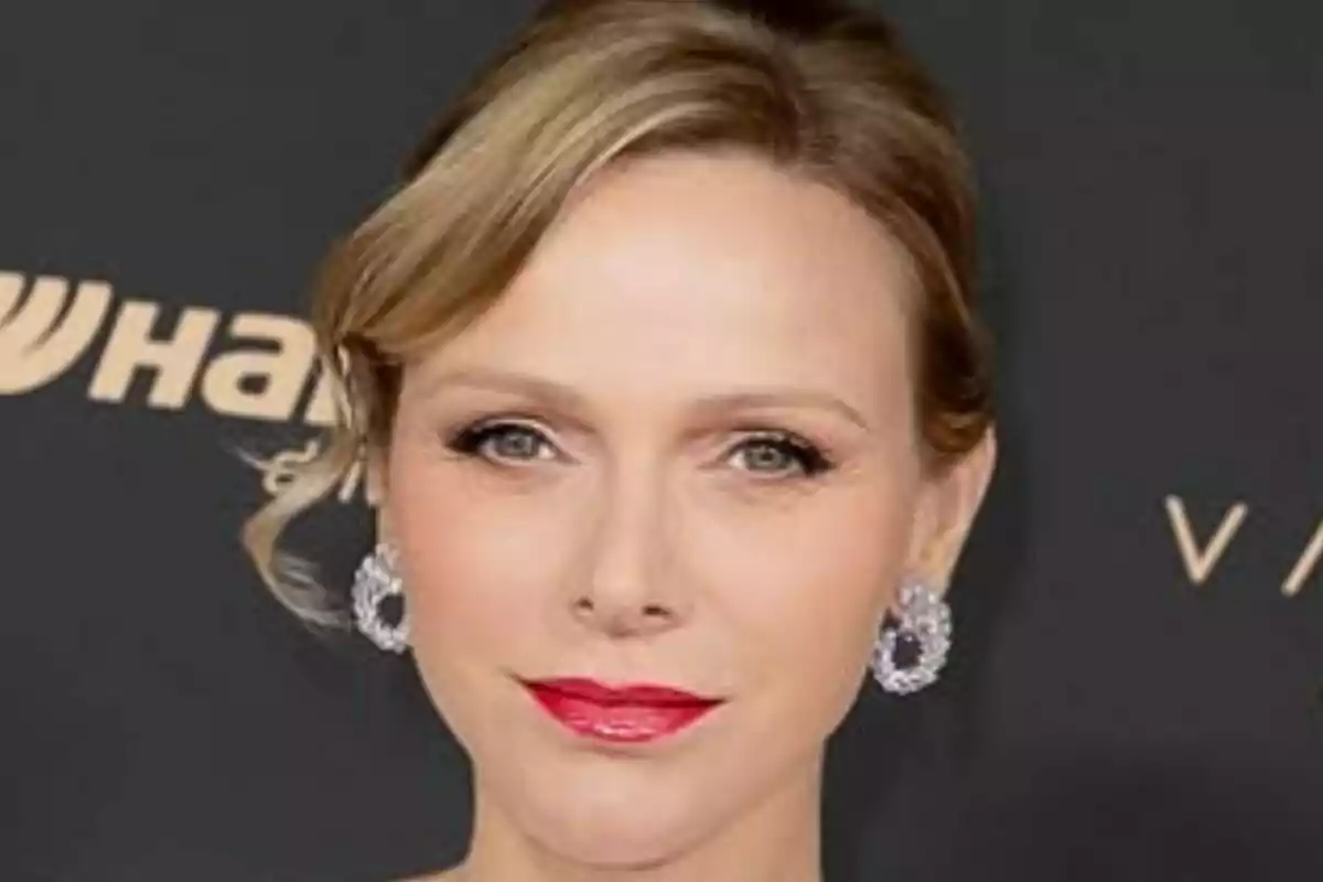 Primer pla de Charlene de Mònaco amb llavis vermells i arracades platejades posant davant d’un fons fosc. Primer pla de Charlene de Mònaco amb llavis vermells i arracades platejades posant davant d’un fons fosc.